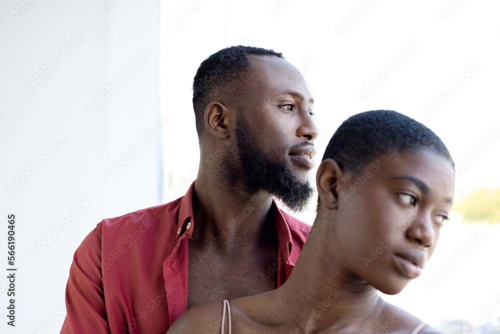 Obraz premium African American couple cuddling with closed eyes near window on sunny day