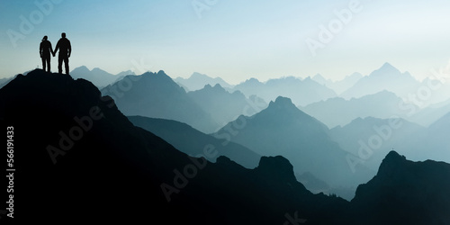 Silhouette Couple of man and woman reaching mountain top enjoying freedom and looking towards blue mountain silhouettes and sunrise. Alps  Allgaeu  Bavaria  Germany.