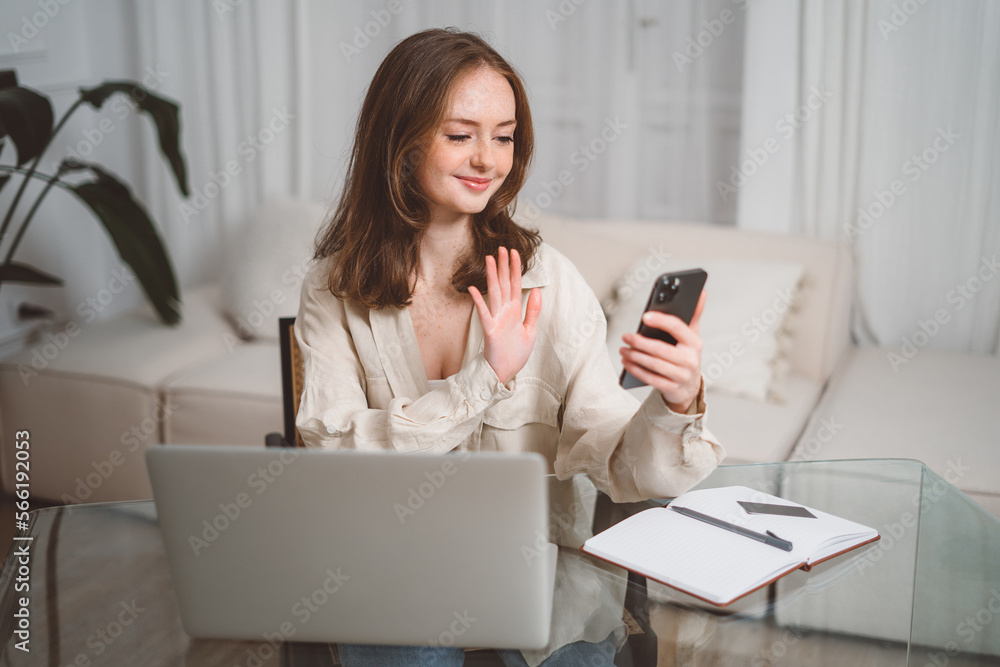 Happy young business woman employee, hr manager having remote online work hybrid meeting or distance job interview waving hand looking at laptop during virtual video conference call in office Happy young business woman employee, hr manager having remote online work hybrid meeting or distance job interview waving hand looking at laptop during virtual video conference call in office