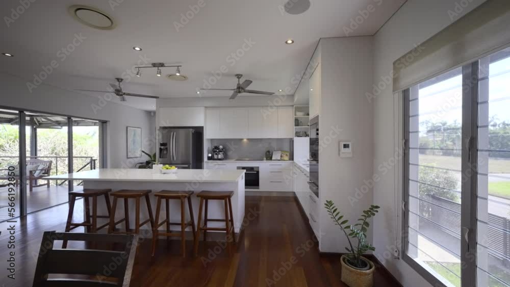 Contemporary home, kitchen, dining room into living room. Family area. White stone bench tops and cupboards. Clean crisp styled home. Lounge room. fans spinning. wooden floor boards Contemporary home, kitchen, dining room into living room. Family area. White stone bench tops and cupboards. Clean crisp styled home. Lounge room. fans spinning. wooden floor boards