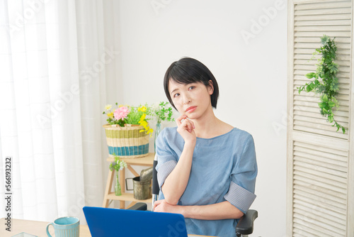 家でパソコンの前で考える車椅子に乗った障がい者女性