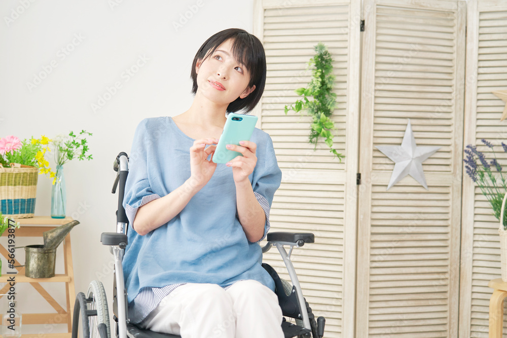 家でスマホを持って想像する車椅子に乗った障がい者女性 家でスマホを持って想像する車椅子に乗った障がい者女性