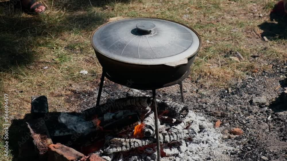 The cauldron of pilaf is prepared on fire. The male hand in the glove closes the hot cover. Hot dish in nature, lunch is ready. Rice, carrots, onions. They interfere with the ladle food. High quality The cauldron of pilaf is prepared on fire. The male hand in the glove closes the hot cover. Hot dish in nature, lunch is ready. Rice, carrots, onions. They interfere with the ladle food. High quality