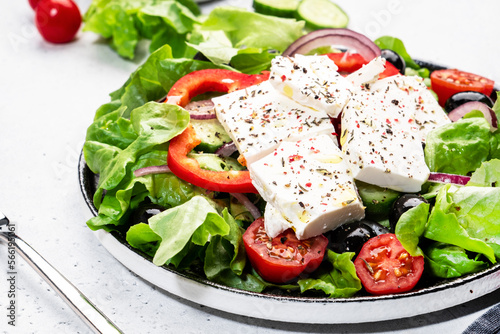 Greek salad with feta cheese, black olives, tomatoes, paprika, cucumber and red onion, healthy vegetarian mediterranean diet food. White background, top view