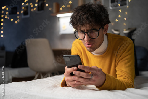 Upset confused young man holding cellphone having problem with mobile phone or missed call, frustrated angry guy student reading bad news in message looking at smartphone annoyed by spam.