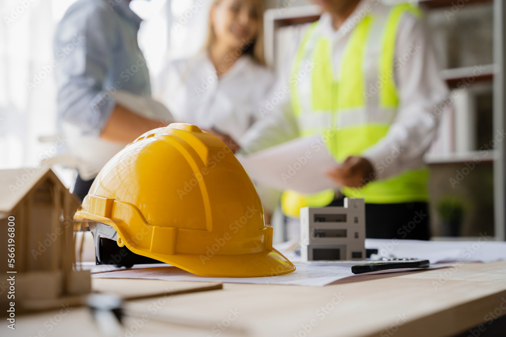 Yellow hard hat on workbench with Engineer teams meeting working together wear worker helmets hardhat on construction site. Asian industry professional team Yellow hard hat on workbench with Engineer teams meeting working together wear worker helmets hardhat on construction site. Asian industry professional team