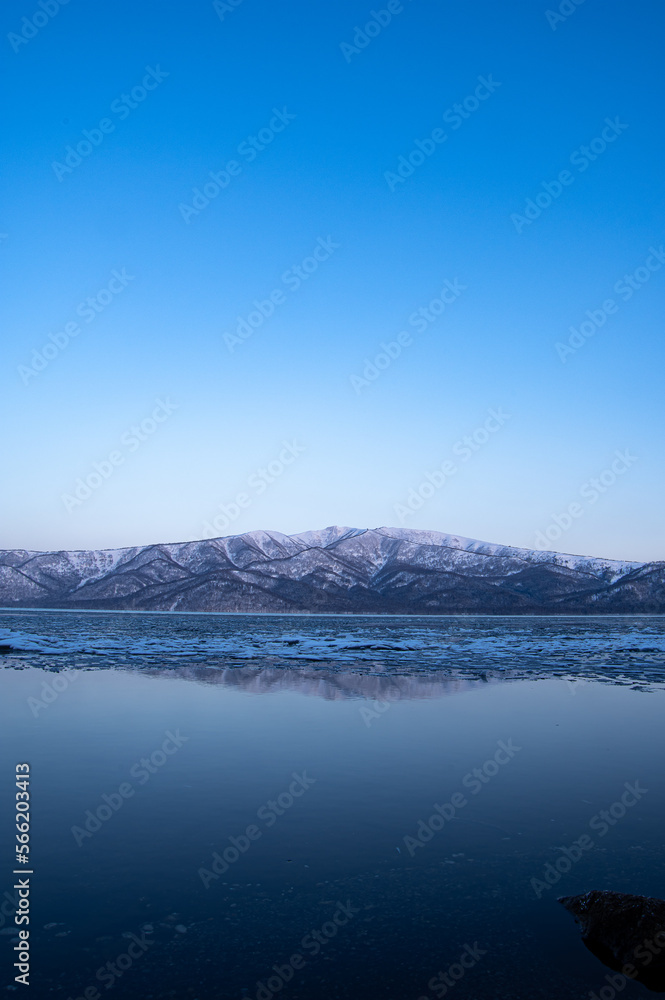 雲の無い青空の下、凍った湖の向こうに見る雪山。