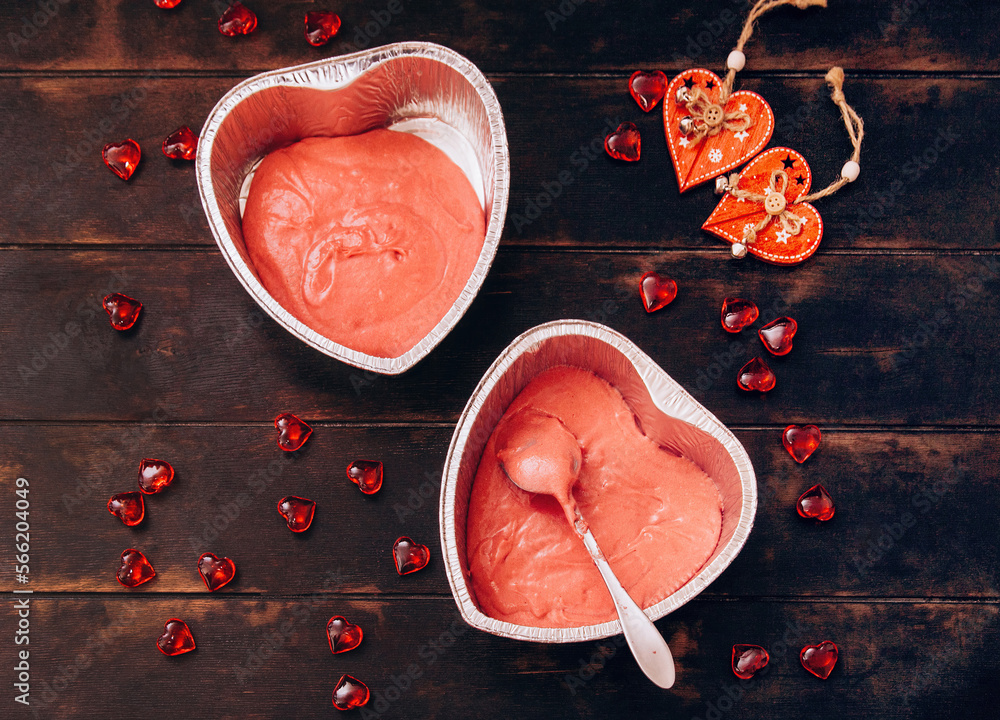 Fototapeta premium Two foil molds with red heart-shaped cake dough. Preparation for Valentine's Day