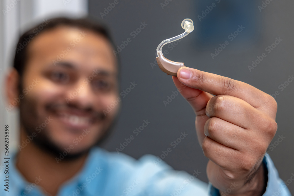 Smiling young man holding a hearing aid Smiling young man holding a hearing aid