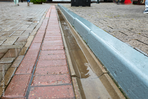 Rainwater runoff during rain. Concrete gutter for rainwater drainage between the sidewalk and the roadway. Selective focus