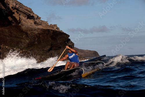 One man paddling an outrigger canoe next to big cliffs and crashing waves.