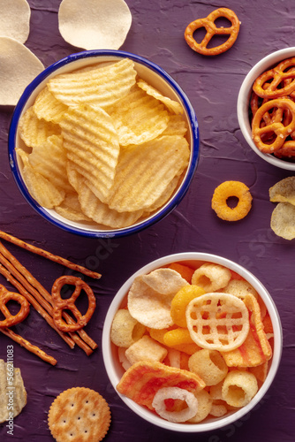 Potato chips and other salty snacks, shot from the top. Party food, shot from above on a purple background. A mix of appetizers in bowls