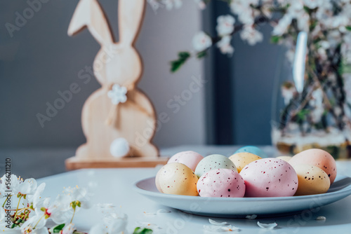 Wall Mural Wooden Easter bunny with blooming tree branches in vase and colored easter eggs i on the plate on the white kitchen table with flower petals