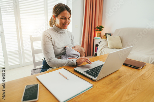 Young mother working at home while feeding her infant son - Smart working and family concept - Focus on mom face