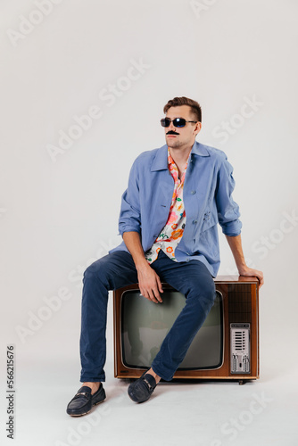 Back in time 90s 80s lifestyle concept. Studio footage of stylish cheerful young man in vintage retro jacket with antique old tv, candy-colored fashions, creativity, emotions, facial expression