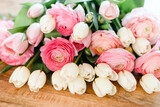 Bouquet of white tulips and pastel pink and peach ranunculus on a wooden table.