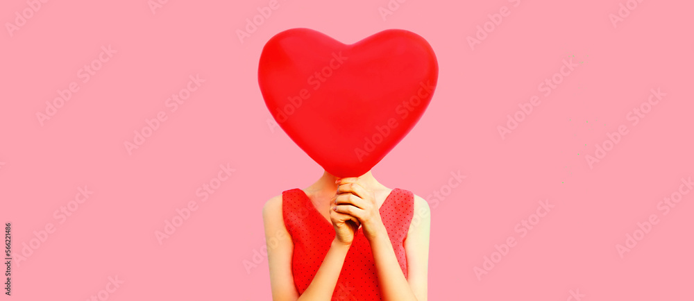 Woman covering her head with big red heart shaped balloon on pink background