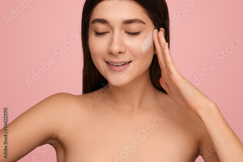 Glad woman smearing cream on cheek