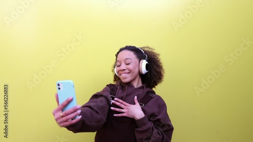 Cheerful young generation z woman taking selfie on smartphone on yellow background. Device addicted young african american woman photographing and smiling. Lifestyle and videoblog addiction. photo