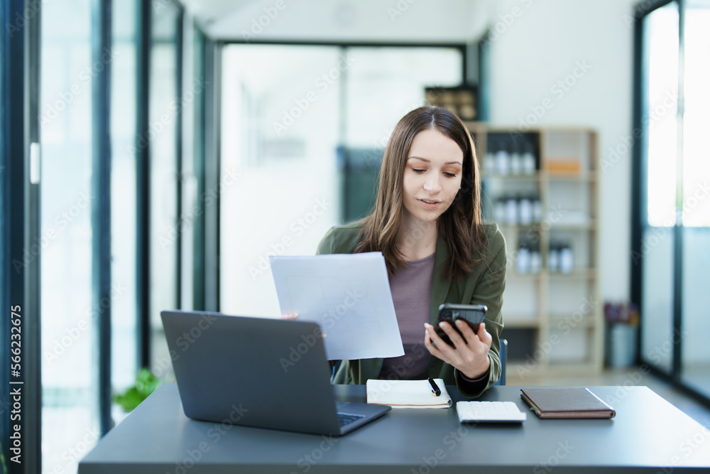 Portrait of a young Asian woman showing a smiling face as she uses his phone, computer and financial documents on her desk in the early morning hours Portrait of a young Asian woman showing a smiling face as she uses his phone, computer and financial documents on her desk in the early morning hours