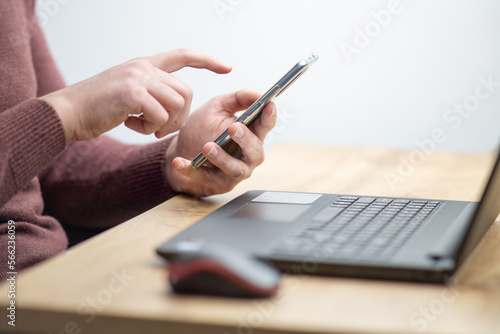 Close up of a man working on laptop and using smartphone. Businessman using smartphone while working on laptop in the office on a desk