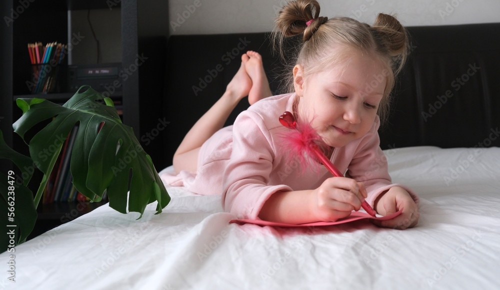Fototapeta premium A child writes a valentine card on the bed with a pen with a heart. The concept for Valentine's Day in children. Valentines child