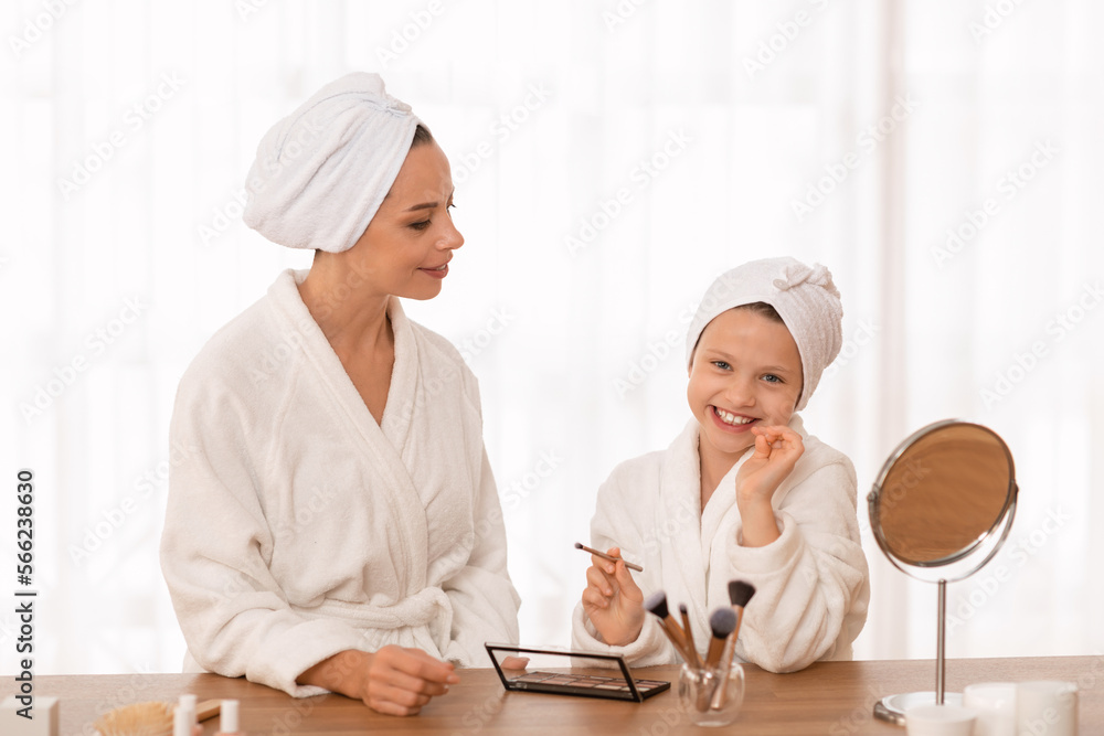 Beautiful mother and her little daughter in bathrobes doing makeup at home