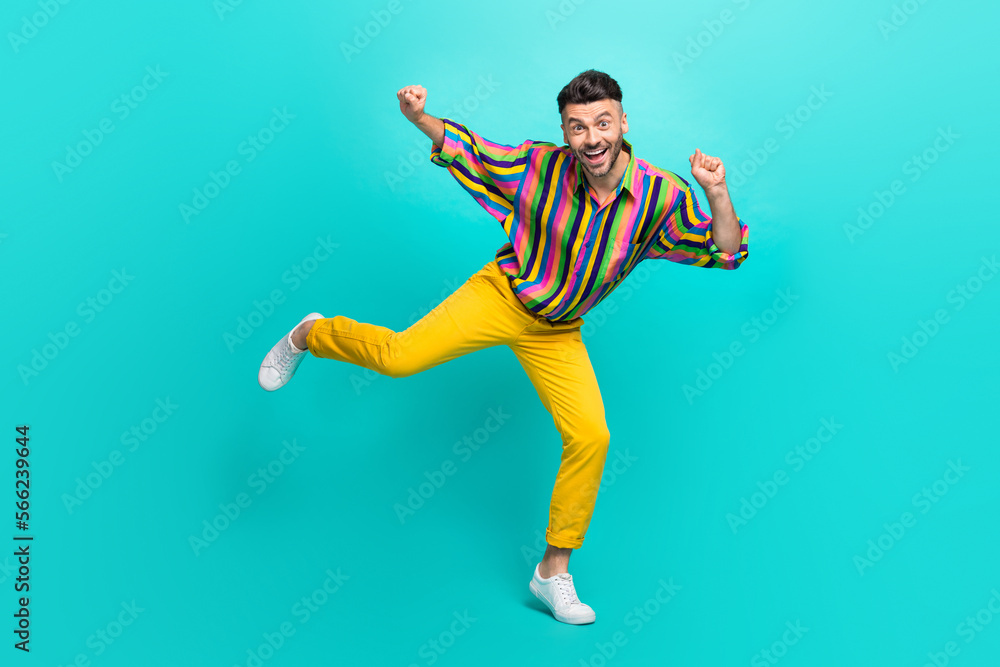 Obraz premium Full length photo of satisfied man dressed striped shirt yellow pants dancing clenching fists isolated on turquoise color background