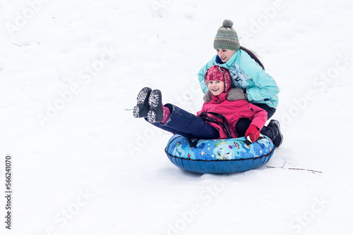 Two happy girls-sisters ride down a winter slide on a children's tubing "cheesecake".
