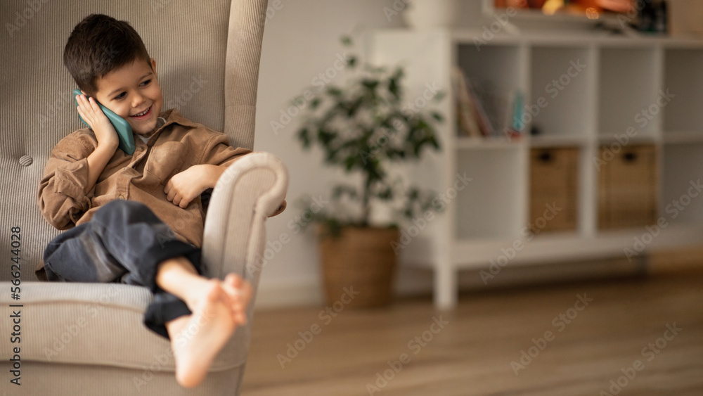 Smiling small european boy sit on armchair calling by phone, talking to parents in room interior, panorama Smiling small european boy sit on armchair calling by phone, talking to parents in room interior, panorama
