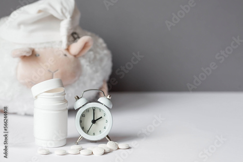 A tube of pills, a sheep in a sleep cap and an alarm clock. The time on the clock is 2 am. Insomnia and recovery of sleep mode. Count sheep to fall asleep. photo