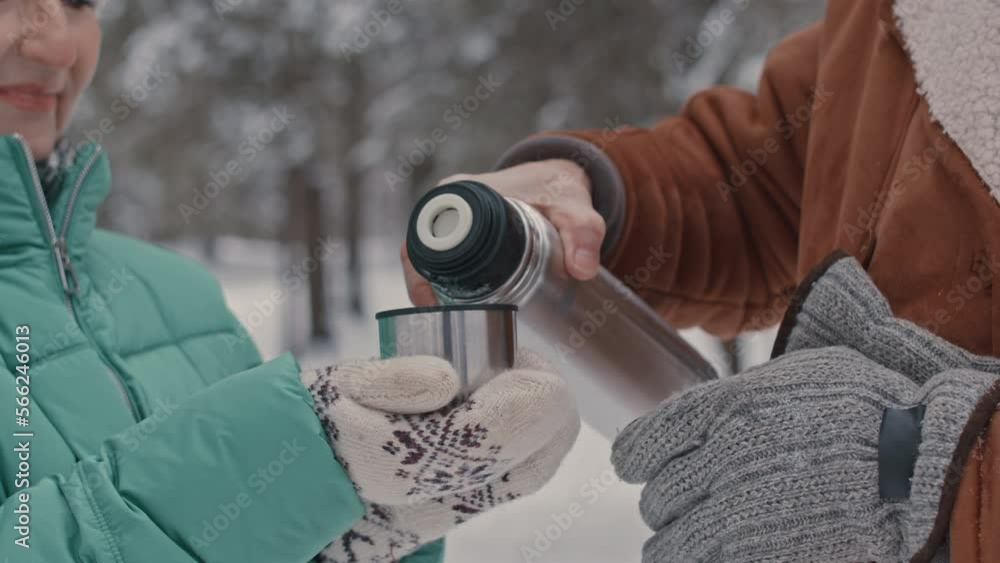 Cropped shot of happy elderly couple drinking tea from thermos during walk outdoors in winter forest Cropped shot of happy elderly couple drinking tea from thermos during walk outdoors in winter forest