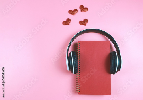 flat lay of red notebook covered with headphones on pink background decorated with red glitter hearts , copy space. Audio book, podcast, .love diary, valentine's day.