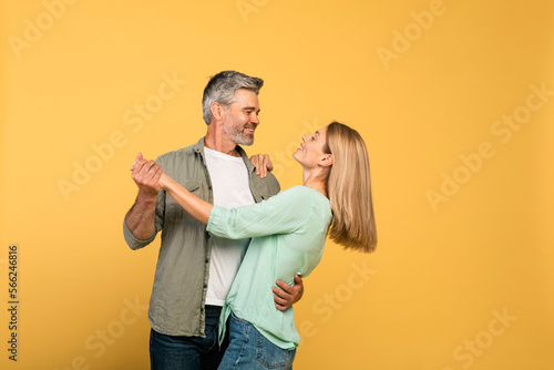 Fotografie Loving middle aged spouses dancing and having fun over yellow studio background,