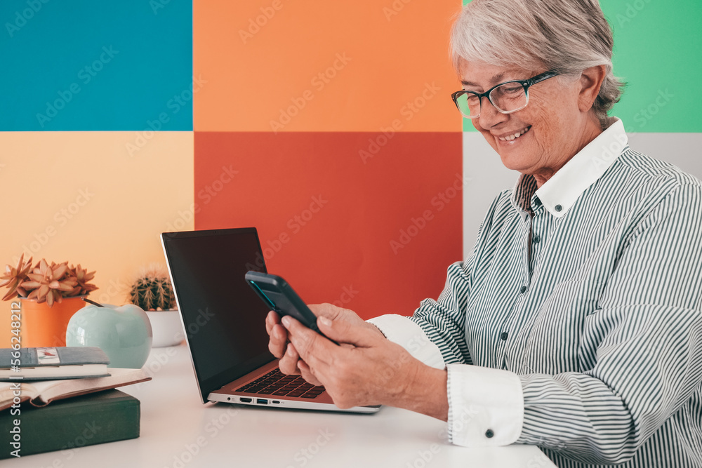 Attractive senior woman in shirt and glasses sitting at office desk using smartphone. Businesswoman smiling working Online, internet banking, wireless technology. Copy space Attractive senior woman in shirt and glasses sitting at office desk using smartphone. Businesswoman smiling working Online, internet banking, wireless technology. Copy space