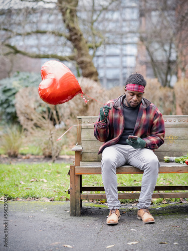 Man with heart shaped balloon sitting on bench