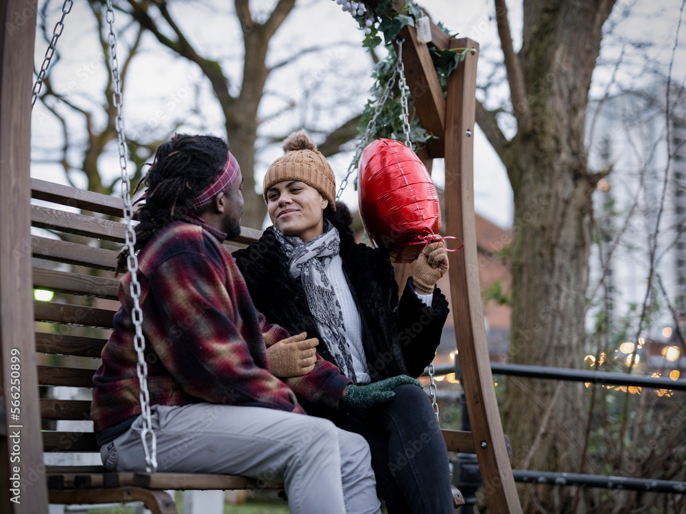 Smiling couple with heart shaped balloon sitting on swing Smiling couple with heart shaped balloon sitting on swing