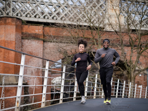 Fotografie Smiling athletic man and woman jogging on footbridge
