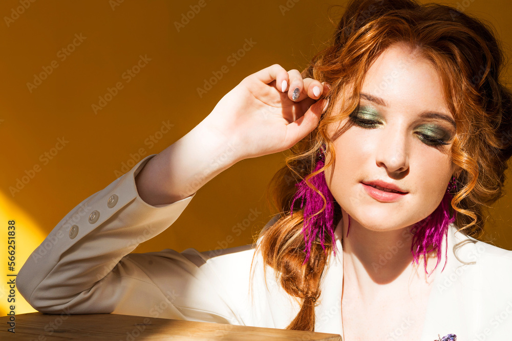Long purple ostrich feather earrings and beetle brooches on a red-haired girl in a white jacket. Girl posing on orange background in sunny weather Long purple ostrich feather earrings and beetle brooches on a red-haired girl in a white jacket. Girl posing on orange background in sunny weather