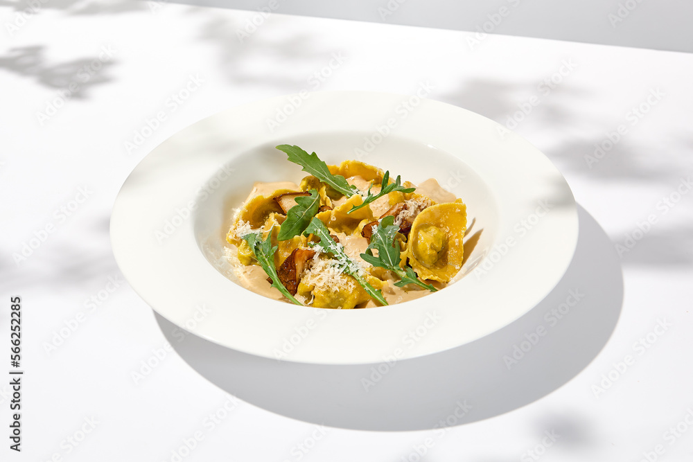 Italian ravioli with meat and mushroom sauce on white plate. Meat tortellini with creamy sauce in summer menu with shadows of tree leaves Ravioli stuffed beef in elegant style Italian ravioli with meat and mushroom sauce on white plate. Meat tortellini with creamy sauce in summer menu with shadows of tree leaves Ravioli stuffed beef in elegant style