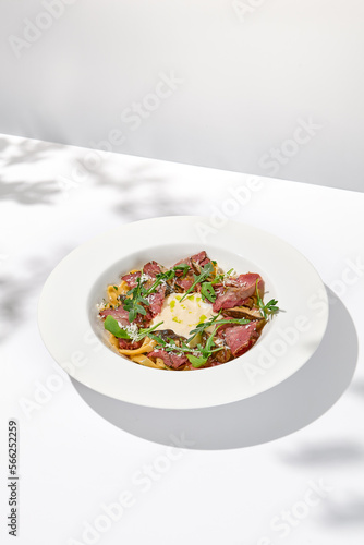Homemade pasta with pastrami and creamy sauce with cheese. Italian pasta pappardelle with beef and sauce on white table Italian food in summer dining with shadows of sunlight