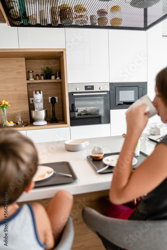 Little boy sitting at the kitchen table while his sister drinks from her mug