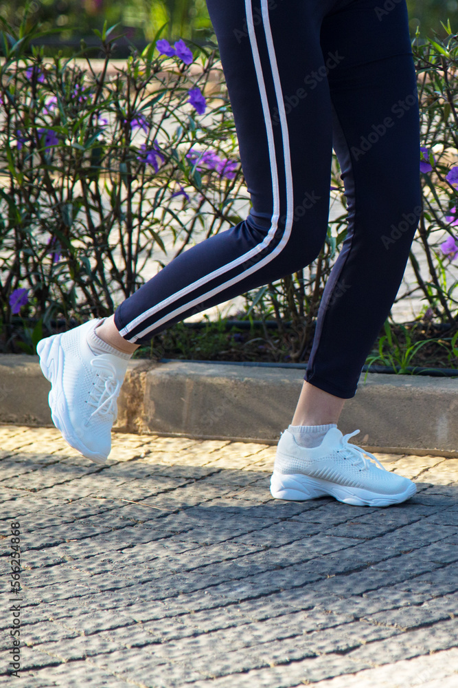 legs of a woman in white sneakers running along rocky path along ...