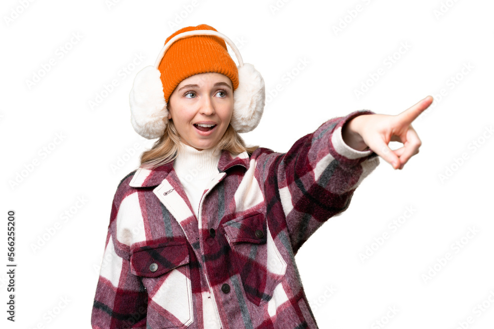 Young  English woman wearing winter muffs over isolated background pointing away