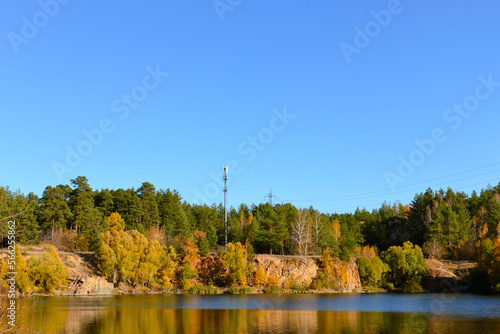 Autumn forest and communication tower on a high rocky shore of the lake