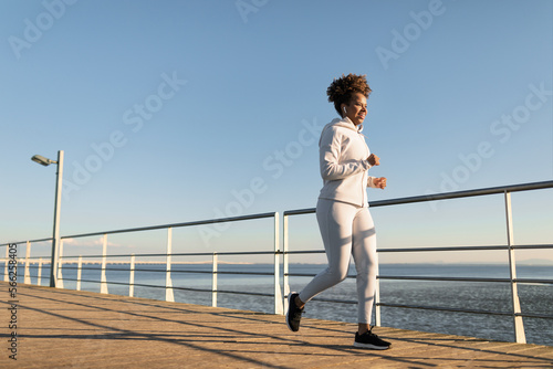 Sporty Young African American Woman In Activewear Jogging Outdoors On Wooden Pier