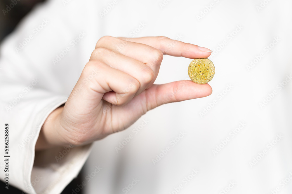 Close-up of a woman holding a pill, a herbal capsule in her hand against the background of a white sweater in blur