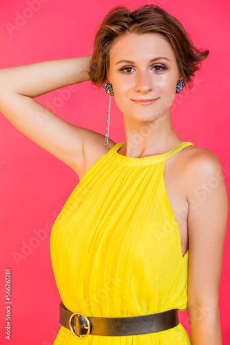 Straight long earrings on a young woman in a yellow dress. Girl posing on a red fuchsia background