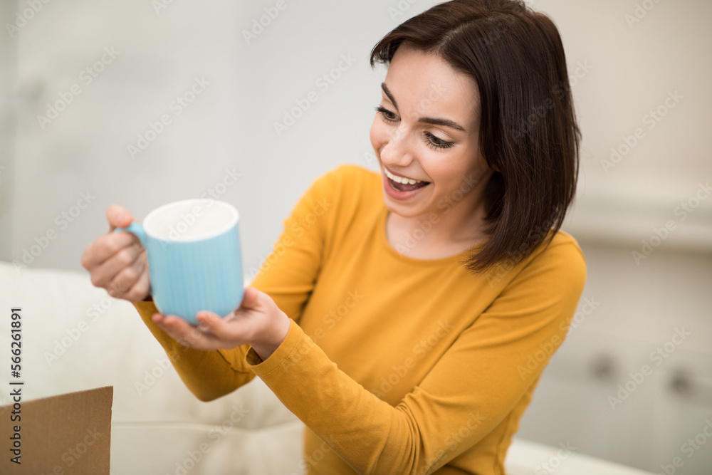 Excited young woman holding blue mug, home interior