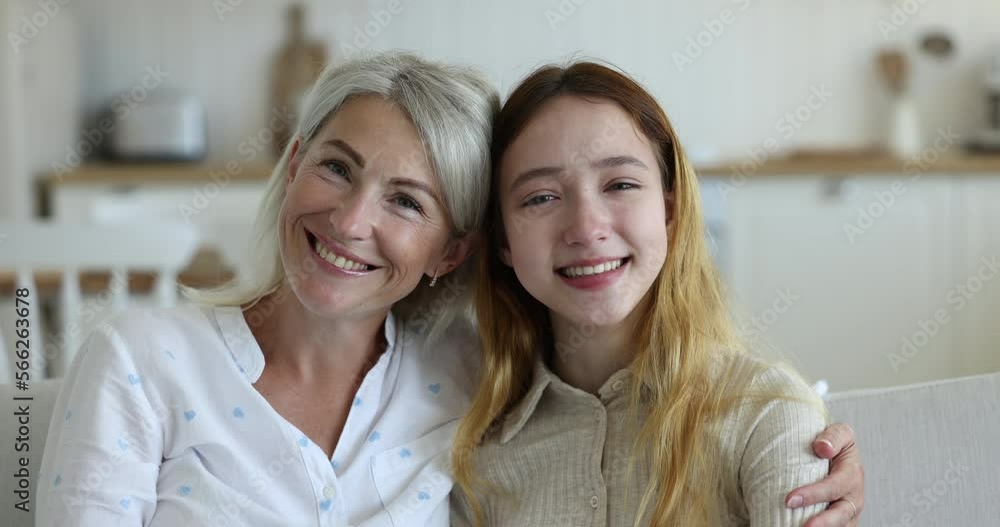 Close up happy faces of loving middle-aged mom and pretty positive teenage daughter smiling look at camera, hugging sit on sofa. Multi-generational women family head shot portrait, bonding and unity Close up happy faces of loving middle-aged mom and pretty positive teenage daughter smiling look at camera, hugging sit on sofa. Multi-generational women family head shot portrait, bonding and unity